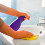 woman doing chores in bathroom at home, cleaning sink and faucet with spray detergent. Cropped view